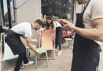 Männliche und weibliche Unternehmer arrangieren Tische und Stühle vor dem Café - MASF22634