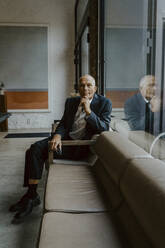 Porträt eines männlichen Unternehmers, der über einem Sofa im Büro sitzt - MASF22645