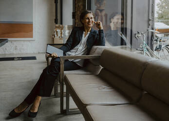 Porträt einer lächelnden Geschäftsfrau, die auf einem Sofa im Büro sitzt - MASF22647