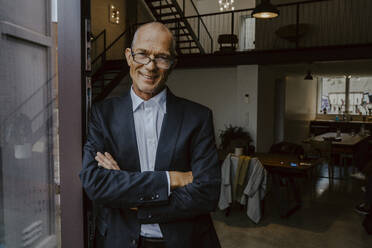 Portrait of smiling businessman with arms crossed at doorway in office - MASF22652