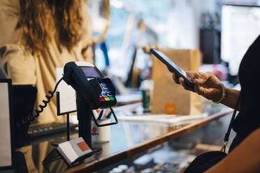 Cropped image of male customer paying through smart phone to female owner at clothing store - MASF22696