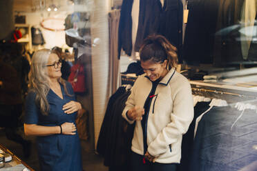 Female customer with warm jacket standing by businesswoman at retail store - MASF22697