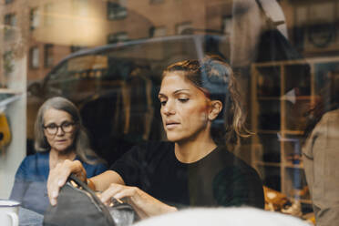 Weibliche Kollegen durch Glas bei der Arbeit in einem Bekleidungsgeschäft gesehen - MASF22702