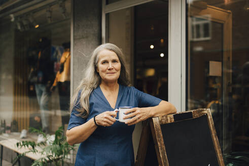 Porträt einer Unternehmerin mit Kaffeetasse vor einem Bekleidungsgeschäft - MASF22708