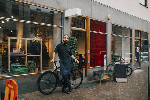 Bärtiger männlicher Besitzer, der vor einer Reparaturwerkstatt am Fahrrad steht - MASF22729