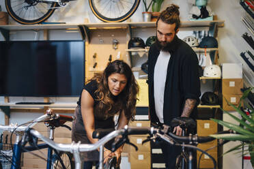 Female owner explaining about bicycle to male customer at retail store - MASF22738