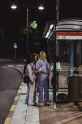 Freundinnen unterhalten sich an einer nächtlichen Bushaltestelle - MASF22741