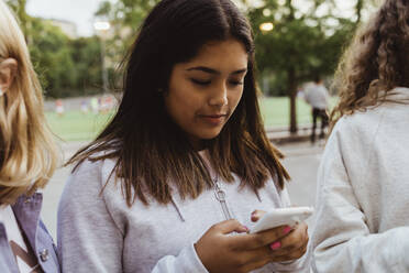 Teenage girl using smart phone with female friends in skate park - MASF22760