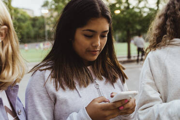 Teenager-Mädchen benutzt Smartphone mit Freundinnen im Skatepark - MASF22760