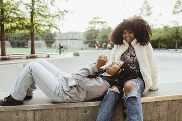 Teenager-Mädchen, das seinen Kopf auf dem Schoß einer Freundin ruht, während es auf einem Skateboard-Park sitzt - MASF22773