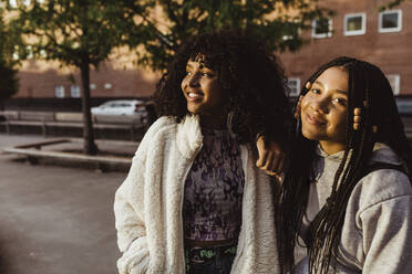 Smiling female teenager friends standing on footpath - MASF22775