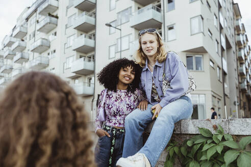 Porträt von lächelnden Freunden an einer Stützmauer in der Stadt - MASF22802