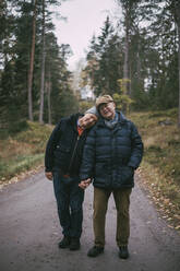 Portrait of senior gay couple standing on road amidst forest - MASF22834