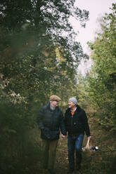 Lächelndes schwules Paar, das sich beim Spaziergang im Wald an den Händen hält - MASF22840