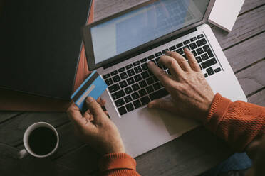 Hände eines älteren Mannes bei der Online-Zahlung mit Kreditkarte über einen Laptop zu Hause - MASF22849