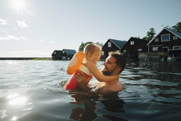 Side view of cheerful daughter with father in lake during vacations - MASF22891