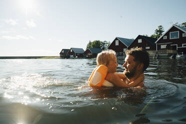 Side view of smiling daughter with father in lake during vacations - MASF22892