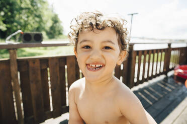Porträt des hemdlosen süßen Jungen, der an einem sonnigen Tag gegen ein Geländer steht - MASF22895