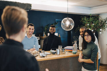 Lächelnde männliche und weibliche Kollegen, die am Tisch in einem kreativen Büro diskutieren - MASF22918