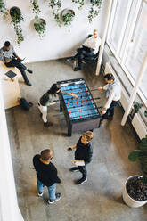 Männliche und weibliche Kollegen spielen Tischfußball, während sie eine Pause von der Arbeit im Büro machen - MASF22932