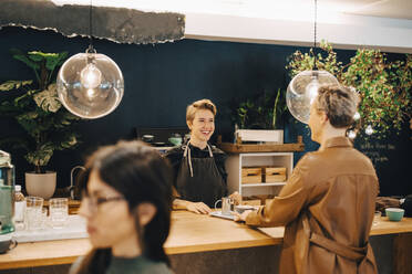 Lächelnde Geschäftsfrau im Gespräch mit einer Kundin am Tisch in einem Café - MASF22963