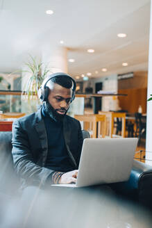 Businessman working on laptop with headphones in office - MASF22979