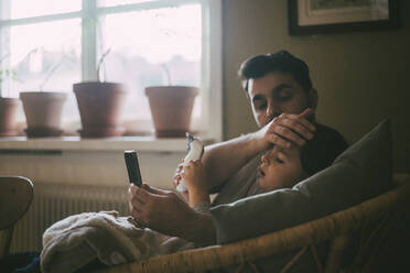 Father checking temperature of son while sitting in living room at home - MASF23005