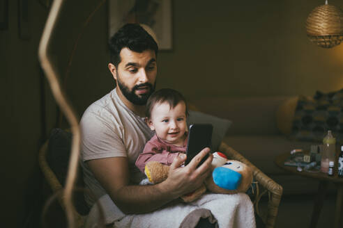 Vater mit Tochter bei der Nutzung eines Smartphones im heimischen Wohnzimmer - MASF23010