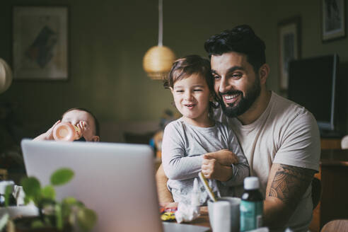 Smiling son and father taking online advice through laptop at home during pandemic - MASF23036