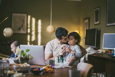 Father kissing son at table in living room - MASF23038