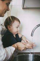 Mutter hilft ihrem kleinen Mädchen beim Händewaschen unter dem Waschbecken in der Küche - MASF23060