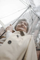 Reife Frau hält Regenschirm an einem regnerischen Tag - VYF00491