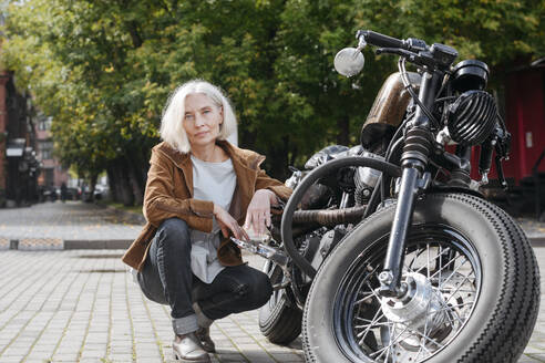 Reife Frau hockt auf einem Motorrad an einem sonnigen Tag - VYF00515