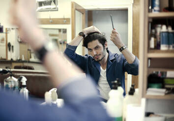 Porträt eines Friseurs, der vor einem Spiegel in einem Friseursalon die Haare frisiert - AJOF01295