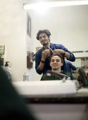 Spiegelung eines Friseurs, der einem männlichen Kunden die Haare schneidet - AJOF01298