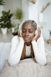Schöne Frau mit geschlossenen Augen hört Musik über Kopfhörer, während sie zu Hause liegt - RCPF00968