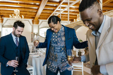 Aufgeregte männliche Freunde halten eine Champagnerflöte beim Tanzen auf einem Bankett - EGAF02262