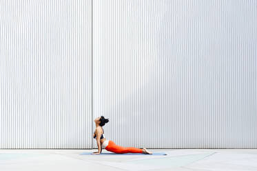 Mid adult female athlete doing cobra pose on mat by wall - PGF00513