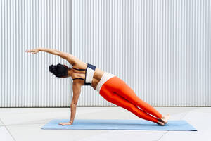 Female sportswoman doing side plank pose in front of wall - PGF00514