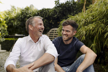 Vater und Sohn lachen, während sie zusammen im Hinterhof sitzen - GUSF05591