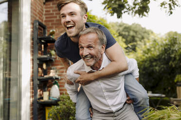 Father giving piggyback ride to son while looking away in back yard - GUSF05598