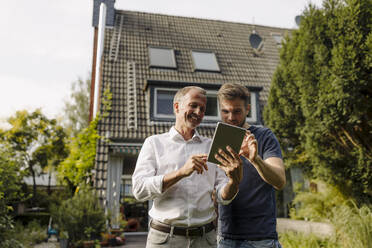 Glücklicher Vater und Sohn benutzen ein digitales Tablet, während sie im Hinterhof stehen - GUSF05602