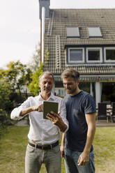 Vater benutzt digitales Tablet, während er neben seinem Sohn im Hinterhof steht - GUSF05603