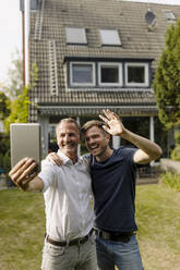 Vater und Sohn führen ein Videogespräch über ein digitales Tablet, während sie im Hinterhof stehen - GUSF05606