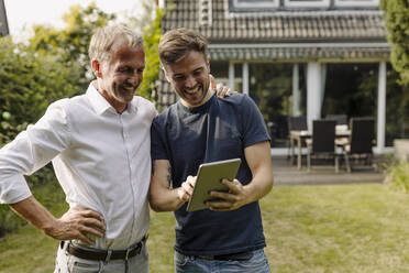 Glücklicher Sohn benutzt ein digitales Tablet, während er neben seinem Vater im Hinterhof steht - GUSF05608