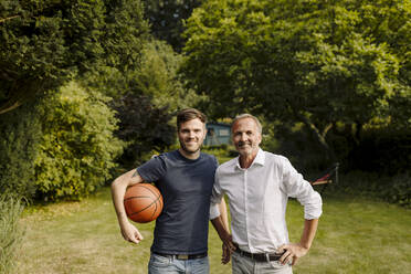 Sohn hält Basketball, während er neben seinem Vater im Hinterhof steht - GUSF05612