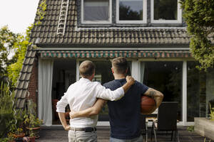 Father and son with arm around standing in front of house - GUSF05613