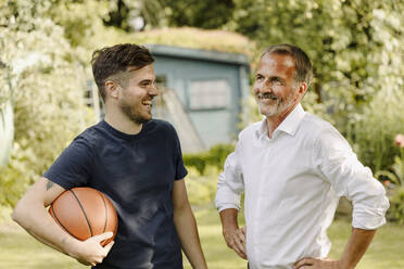 Fröhlicher Sohn mit Basketball, der seinen Vater anschaut, während er im Hinterhof steht - GUSF05614