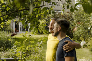 Son and father looking away while standing in back yard - GUSF05617