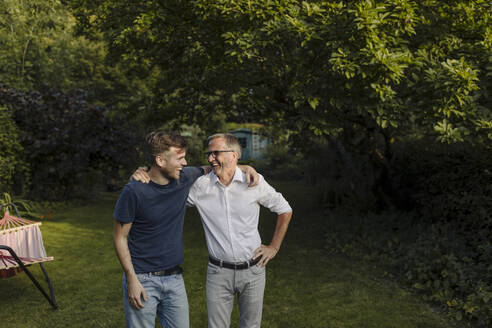 Laughing son and father with arm around standing in back yard - GUSF05648